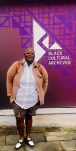 Jes Neal standing in front of a wall that says Black Cultural Archives