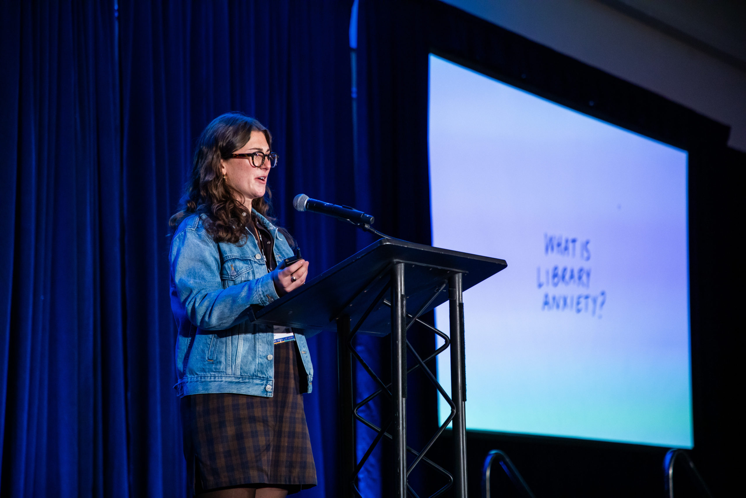 Person standing at podium speaking with slidehow in background on screen.